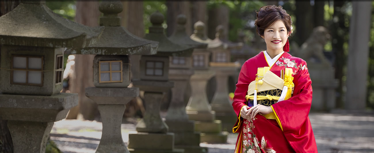 神社の灯籠の前に立つ赤い振袖姿の女性